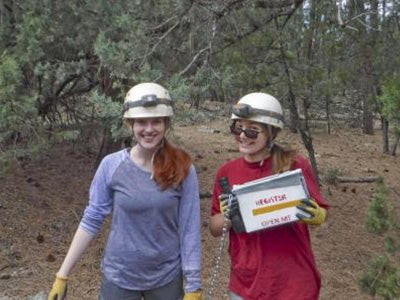 Two female students wearing cave helmets, hold a register cave box.