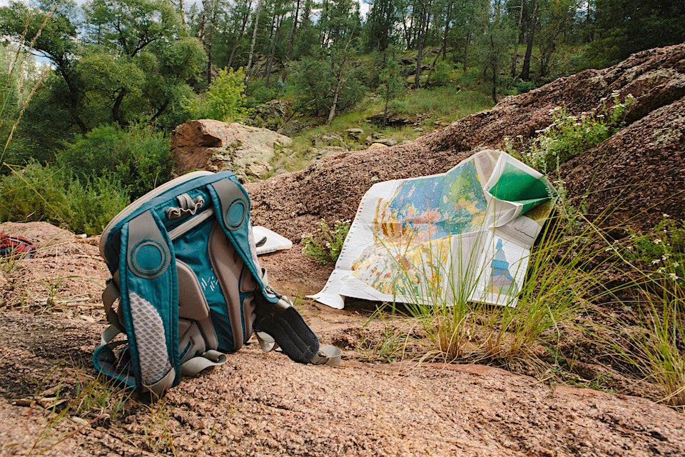 A lone backpack and map lay on a rock, the wilderness of the forest in the background.