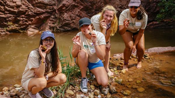 Four female students by a creek stop to show off their rock findings during camp.