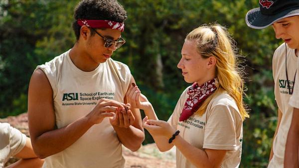 A male and female student wearing their SESE t-shirts compare rock specimens in camp.