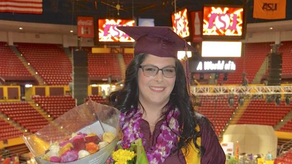 Cassie stands in the ASU auditorium wearing her graduation attire holding a bouquet of flowers.