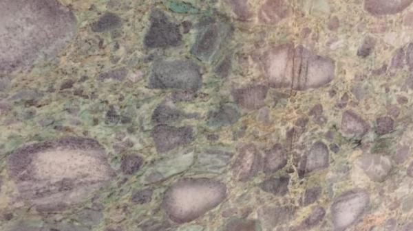 A close up of a slab composed of variably rounded clasts (cobbles and pebbles) in shades of green and purple.